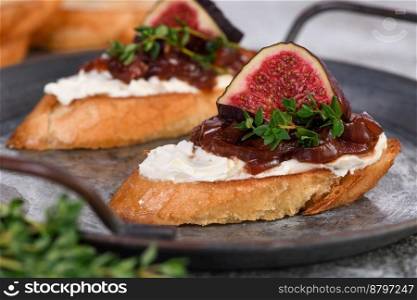 Canape or crostini with toasted baguette, cream cheese, onion jam, figs and fresh thyme on a tin tray. Ideal appetizer as an aperitif.
