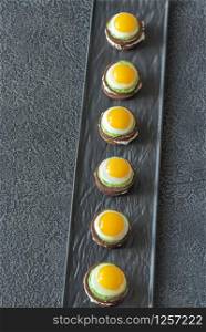 Canape with cream cheese, guacamole and fried quail eggs on the plate
