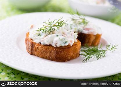 Canape with soft cheese spread on white plate, close up, selective focus