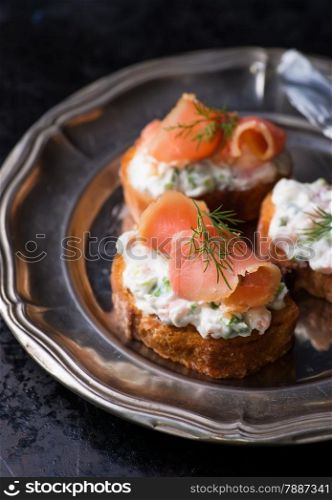 Canapes with smoked salmon and cream cheese on vintage metal plate, selective focus