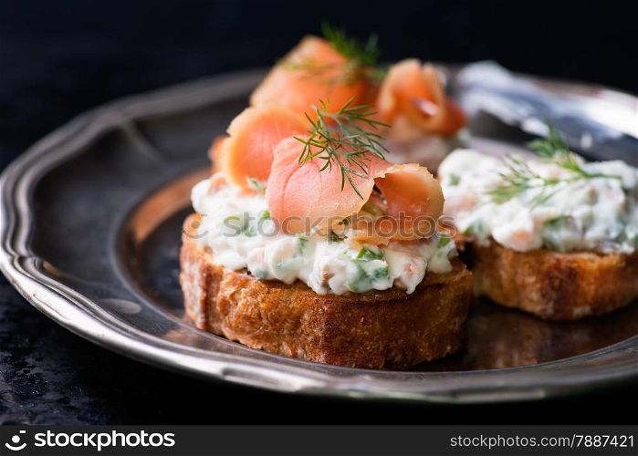 Canapes with smoked salmon and cream cheese spread on vintage metal plate, selective focus