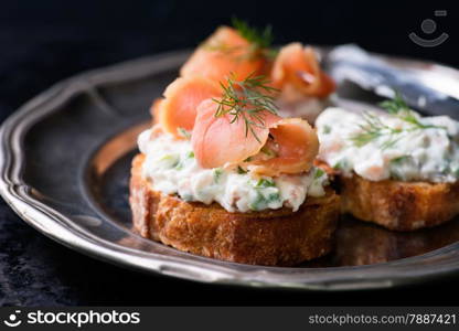 Canapes with smoked salmon and cream cheese spread on vintage metal plate, selective focus