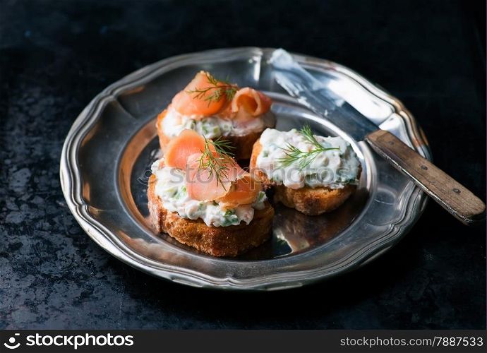 Canapes with smoked salmon and cream cheese spread on vintage metal plate, selective focus