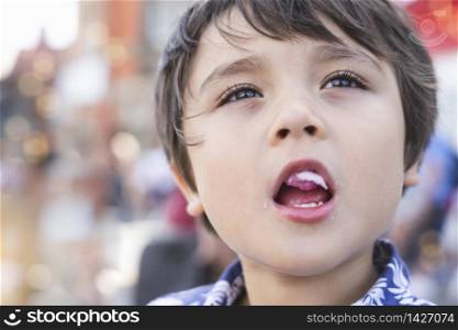 Candid head shot of cute little boy eating candy floss with blurry street bokeh background, Young boy with deep in though while eating cotton candy, Concept of the international children&rsquo;s day.