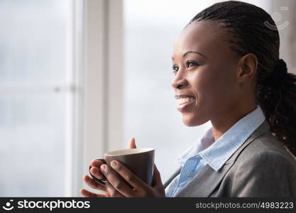 Candid image of a businesswoman drinking coffee while working at office. Selective focus.