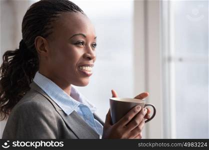 Candid image of a businesswoman drinking coffee while working at office. Selective focus.