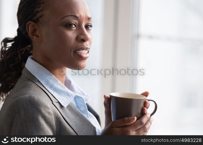 Candid image of a businesswoman drinking coffee while working at office. Selective focus.