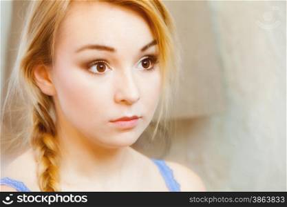 Candid portrait of pensive young woman with blond braided hair. Face of thoughtful teenage girl. Indoor.