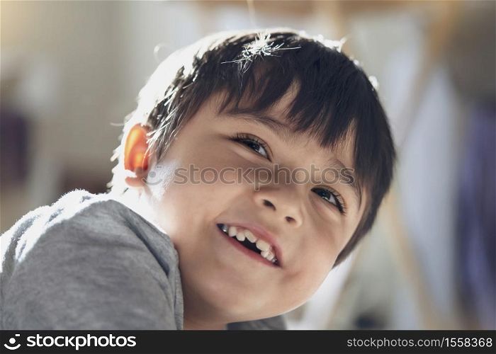 Candid shot happy kid looking up with smiling face, High key light healthy child relaxing at home, Positive Little boy having fun on his own with blurry sunny light background.