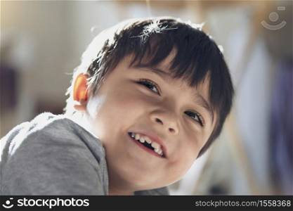 Candid shot happy kid looking up with smiling face, High key light healthy child relaxing at home, Positive Little boy having fun on his own with blurry sunny light background.