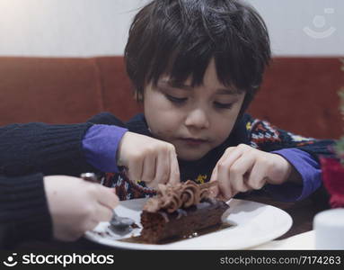 Candid shot humgry kids eating chocolate cake in the cafe, Cute little boy emjoy eating dessert for snack time.