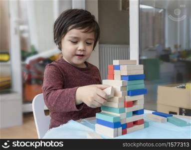 Candid shot of cheerful little boy plays colourful wooden blocks in play room, Portrait of child stacking wooden blocks at home, Educational toys for preschool and kindergarten child. Creative concept