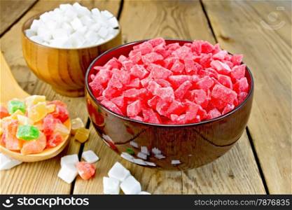 Candied papaya and coconut in bowls, colorful pieces of candied fruit in a spoon on a wooden board
