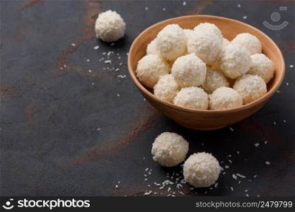 Candies in coconut flakes bowl on dark table background