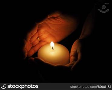 candle and hands on a black background. candle and hands on a black background