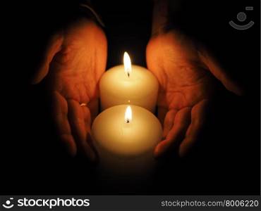 candle and hands on a black background. candle and hands on a black background