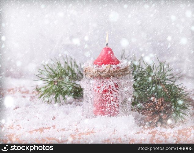 Candle, cones and spruce branches on a snow-covered wooden background