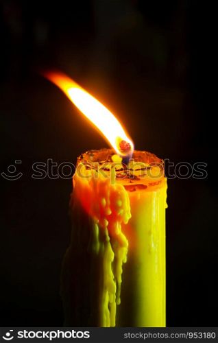 Candle flame close up on a black background. Single light flame candle or beeswax candle burning brightly on black background.