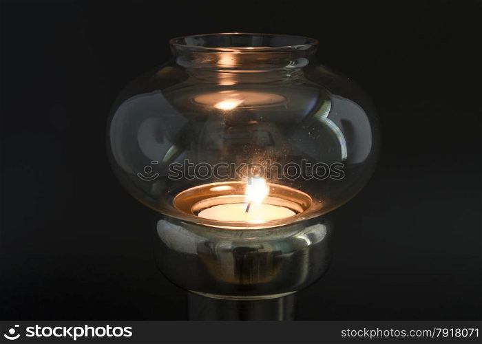 Candle flame in glass topped antique lamp, in darkened area.