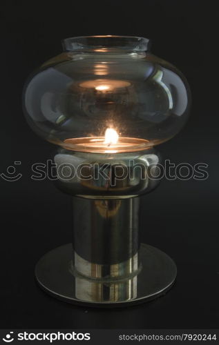 Candle flame in glass topped antique lamp, in darkened area.