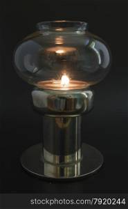 Candle flame in glass topped antique lamp, in darkened area.