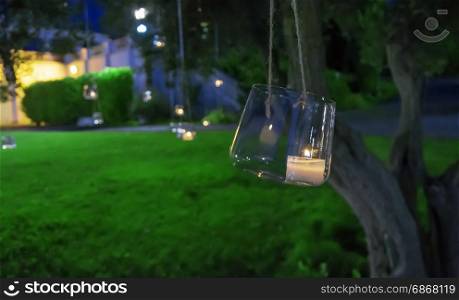 candle in a glass hanging from a tree in a formal garden