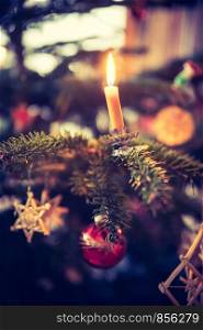 Candle on a branch of a decorated Christmas tree