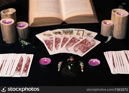 Candles and old tarot cards on black silk. Halloween and fortune telling concept. Mystic background with occult and magic objects on witch table.