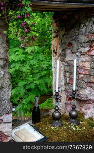 Candles in a candlestick, bottle of ch&agne and two glasses in moss at stone ruins. Wedding celebration simbols in outdoors. 