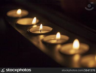 Candles in a row in a long candle holder, focus on center, in darkness, horizontal image