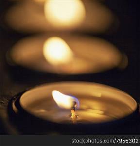 Candles in row, in darkness, focus on first candle, strict depth of field, square image