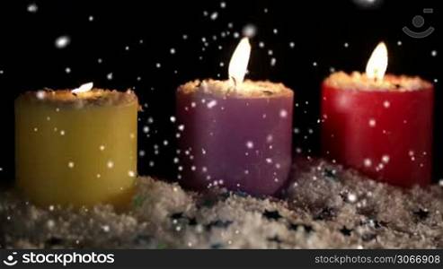 Candles isolated on black. Snow is falling. Holiday background with copyspace for text.