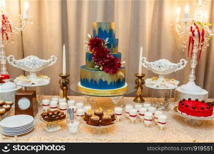 Candy bar. blue wedding cake decorated by flowers standing of festive table with deserts, strawberry tartlet and cupcakes. Wedding. Reception Tartlets. Candy bar. blue wedding cake decorated by flowers standing of festive table with deserts, strawberry tartlet and cupcakes. Wedding.