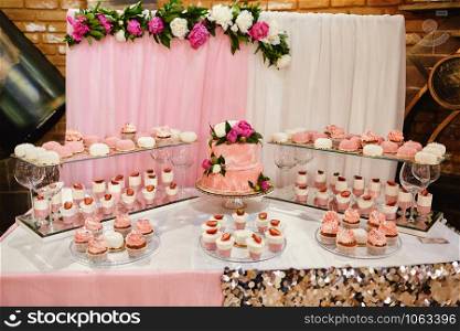 Candy bar. Pink wedding cake decorated by flowers standing of festive table with deserts, strawberry tartlet and cupcakes. Wedding. Candy bar. Pink wedding cake decorated by flowers standing of festive table with deserts, strawberry tartlet and cupcakes. Wedding.