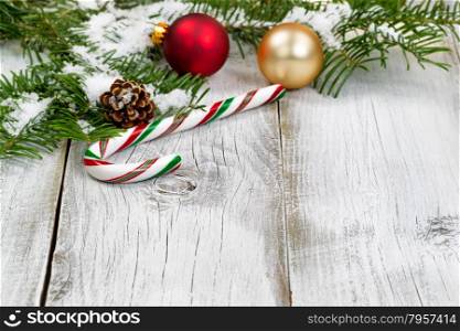 Candy cane with snow covered real Fir tree branches, ornaments, cone and snow on rustic white wooden boards. Christmas season concept. Focus on front part of candy cane.