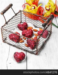 Candy heart shape Valentine Day. Stylish metal basket with candies in shape of heart and bouquet of orchids