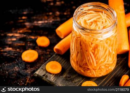 Canned carrots in a jar on a cutting board. On a rustic dark background. High quality photo. Canned carrots in a jar on a cutting board.