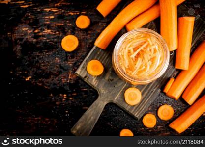 Canned carrots in a jar on a cutting board. On a rustic dark background. High quality photo. Canned carrots in a jar on a cutting board.