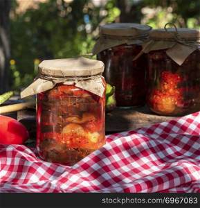 Canned eggplant slices in spicy vegetable sauce in glass jars, close up