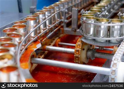Canned fish factory. Food industry. Sardines in red tomato sauce in tinned cans at food factory. Food processing production line. Food manufacturing industry. Many can of sardines on a conveyor belt.