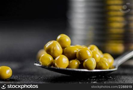 Canned green peas in a spoon. On a black background. High quality photo. Canned green peas in a spoon.