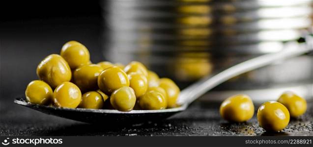 Canned green peas in a spoon. On a black background. High quality photo. Canned green peas in a spoon.