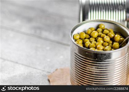 Canned green peas in a tin can on the table. On a gray background. High quality photo. Canned green peas in a tin can on the table.