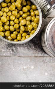 Canned green peas in a tin can on the table. On a gray background. High quality photo. Canned green peas in a tin can on the table.