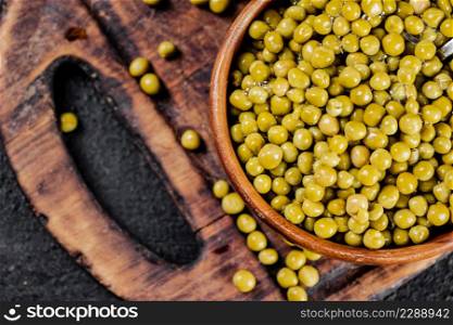 Canned green peas in a wooden bowl. On a black background. High quality photo. Canned green peas in a wooden bowl.