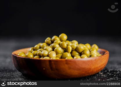 Canned green peas in a wooden plate. On a black background. High quality photo. Canned green peas in a wooden plate.