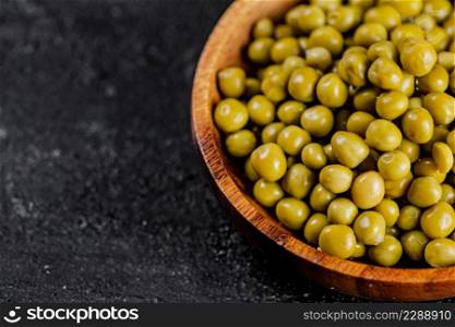 Canned green peas in a wooden plate. On a black background. High quality photo. Canned green peas in a wooden plate.