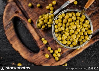 Canned green peas on a cutting board. On a black background. High quality photo. Canned green peas on a cutting board.