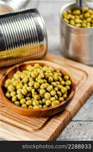 Canned green peas on a wooden cutting board. On a gray background. High quality photo. Canned green peas on a wooden cutting board.