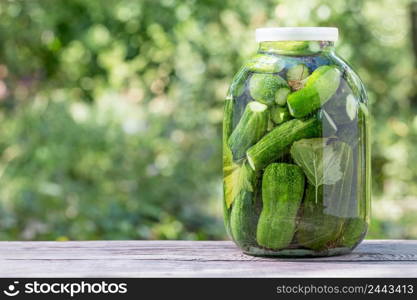 Canned homemade cucumbers in glass jar on wooden table. Natural green background. Canned homemade cucumbers in glass jar on wooden table